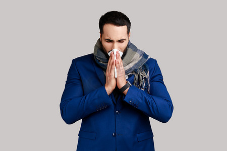 男人裹着温暖的围巾，餐巾打喷嚏，清洁流鼻涕，患有过敏或流感症状