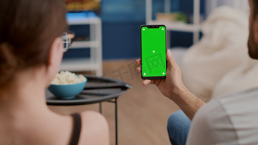 在线对弈摄影照片_在线会议或小组视频通话中夫妇手持绿屏垂直智能手机的特写