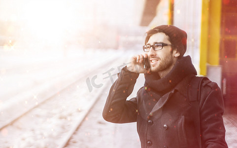 年轻时尚的男人站在地铁站，拿着智能手机