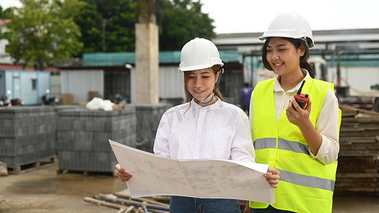 两名戴着安全帽和黄色背心的建筑师女性检查工业建筑施工现场