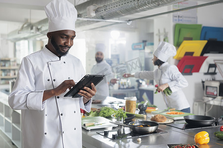 带着手持设备的美食专家站在餐厅专业厨房里寻找晚餐食谱。