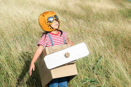 阳光明媚的日子里，可爱的梦想家小女孩在草地上玩纸板飞机。