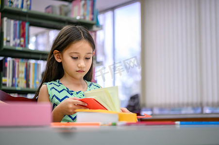 书店的人摄影照片_可爱的小女孩在学校的图书馆里专心读书。