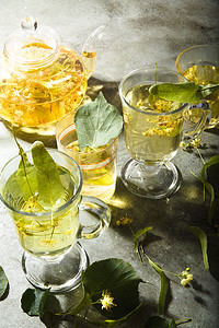 绿色桌子上放着新鲜制作的椴树茶和茶壶，上面有椴树的叶子和花朵。