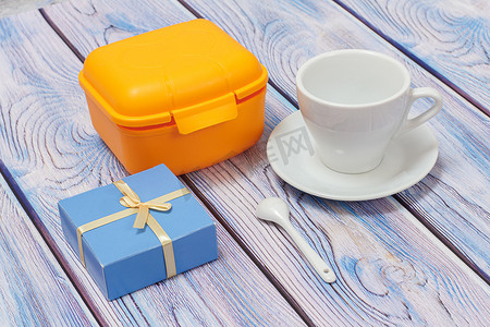 塑料黄色午餐盒、礼品和杯子，木质背景上有茶碟。