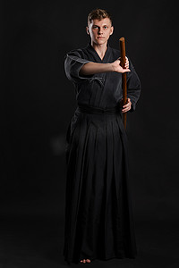 武士背景摄影照片_穿着传统日本和服的剑道大师正在黑色工作室背景下用竹剑练习武术。