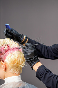 美容院的理发师将女性金发染成粉红色。