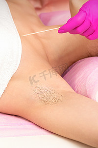 手戴手套，用抹刀在水疗中心为女性毛茸茸的腋窝脱毛。