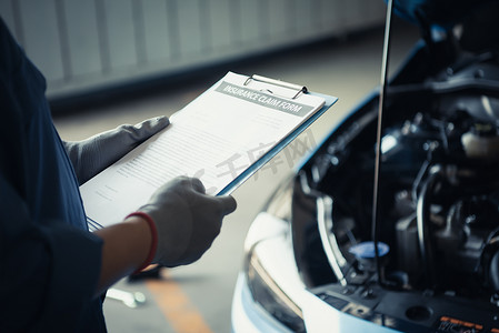 汽车修理工拿着剪贴板，并根据汽车修理店车库的客户保险索赔单检查维修车辆。