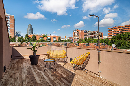 明亮的露台配有黄色外部椅子、木地板、淋浴和波布雷诺地区的壮丽景色，波布雷诺是西班牙巴塞罗那的老工业区，改建为新的现代社区