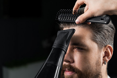 理发师在时尚发型后吹干一位英俊的胡须男子的头发。