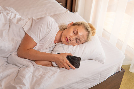 女人睡觉时金发手机漂亮的床毯景观早晨，适合女性白种人，适合人快乐的午睡，房间健康。