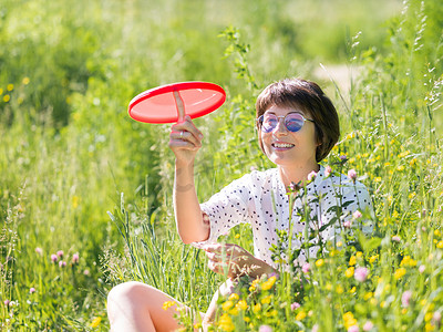 戴着彩色太阳镜的女人玩红色飞盘，在草地上享受阳光和花香。
