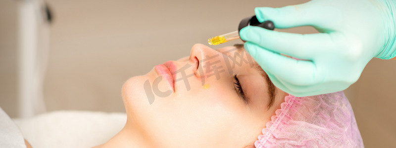 年轻的白人妇女在美容诊所用移液器获取酸性有机视黄醇剥离面部皮肤。