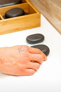 按摩师的手从水疗沙龙的桌子上取出黑色按摩石。