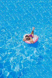 戴着墨镜的苗条女人在泳池里穿着明亮泳衣的充气游泳圈，夏季照片，游泳摄影，夏季女人照片。