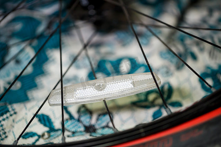 自行车黑色车轮的灰色金属辐条上的一个塑料白色反光镜