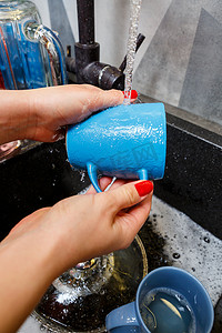 回弹海绵摄影照片_用海绵手在水下洗杯子，家庭主妇用蓝色海绵在厨房水槽里洗蓝色杯子，手清洁，手动，家务洗碗机