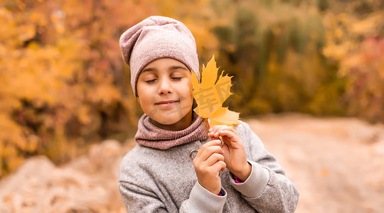 穿着温暖针织围巾在公园或森林里散步的美丽快乐小女孩的秋季户外肖像