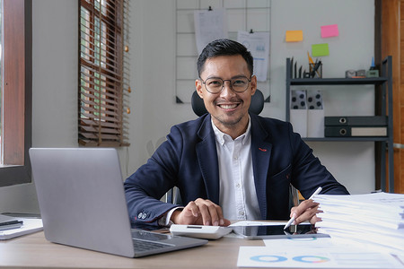 一位男性企业主在工作中使用计算机和财务预算文件成功投资自己的企业时，脸上露出幸福的笑脸。