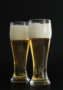 活动气泡摄影照片_两杯冰冷的金色啤酒，黑色背景上有气泡。