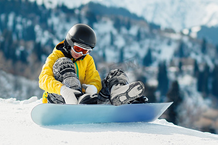 年轻女子滑雪板运动员坐在雪地里，在下降前将紧固件固定在滑雪板上