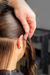 美发师将女性头发分成几部分，用梳子在美发沙龙特写中用手握住头发。