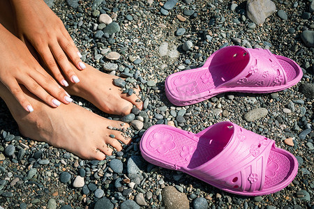 海滩石头背景上的妇女手脚和橡胶拖鞋。