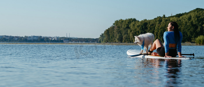狐狸女孩摄影照片_年轻女子与她的狗日本狐狸坐在 Sup 板上，在城市湖上放松