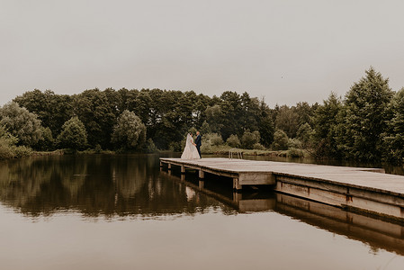 新婚夫妇在湖上的木墩桥上亲吻拥抱