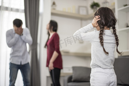 被揪住耳朵的人摄影照片_后视图中，小女孩把手放在耳朵上，因为她不想听到爸爸和妈妈吵架。