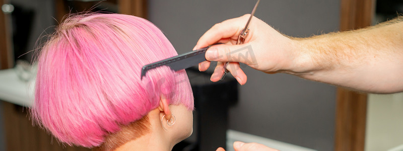 美发师的手在美容院为一位年轻的白人女性梳理头发，制作粉色短发。