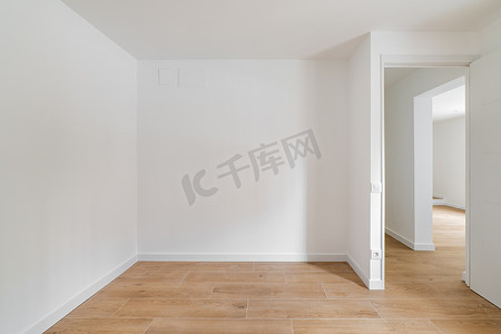 粉刷墙摄影照片_翻新公寓内的空房间配有强化木地板和新粉刷的白色墙壁，走廊通向其他房间。
