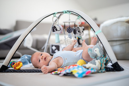 可爱的小男孩在家里的垫子上玩悬挂的玩具拱门 婴儿活动和游戏中心，用于婴儿早期发育。