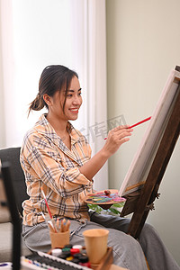 满意的千禧一代女性在明亮的家庭工作室里用水彩画在画布上。