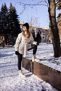一位穿着白色夹克和白色皮靴的漂亮年轻女子在雪地公园里散步