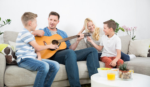 快乐的白人家庭在舒适的现代家里微笑、弹吉他、唱歌