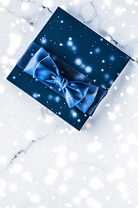 新年新年礼盒摄影照片_冬季节日礼盒，配有蓝色丝绸蝴蝶结、大理石背景上的雪花，作为豪华美容品牌的圣诞和新年礼物，平铺设计