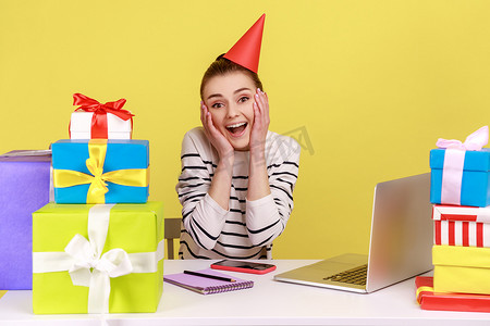 女人坐在工作场所的礼盒中间，戴着派对锥，在工作中庆祝生日