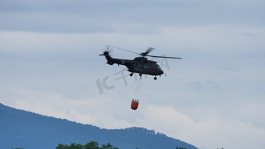 消防直升机携带装满水的吊桶飞行以扑灭火灾