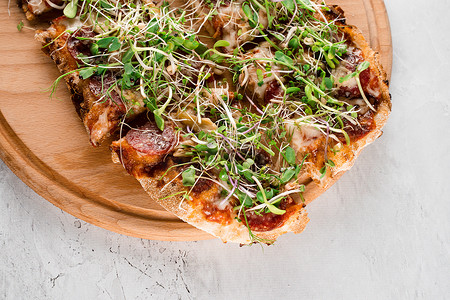 Pinsa romana 配萨拉米香肠、奶酪、蘑菇，在白色背景的木板上用微绿装饰。