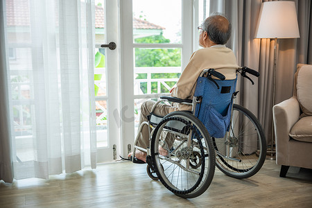 亚洲老人残疾独自坐在轮椅上，透过医院的窗户望去