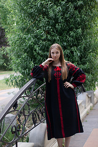 临夏民族大剧院摄影照片_迷人的乌克兰年轻女子在户外穿着民族红色和黑色刺绣连衣裙。
