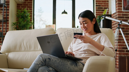 电脑凭证摄影照片_快乐的年轻成年女性在购物网站上插入信用卡凭证以进行在线支付