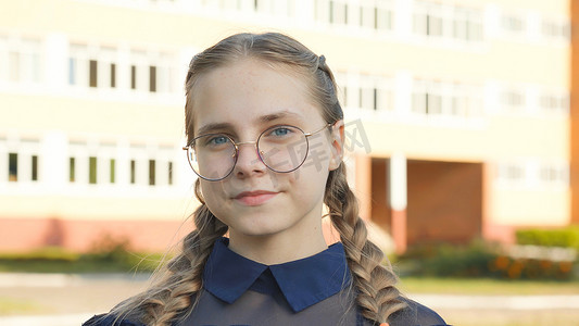 戴眼镜的青少年人摄影照片_一名戴眼镜的少女在学校门前。