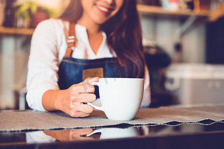 加奶咖啡杯特写镜头有美丽的亚洲女咖啡师背景的为顾客服务。