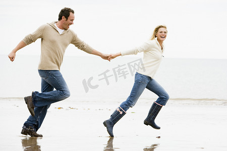 牵手奔跑摄影照片_情侣牵手微笑在海滩上奔跑