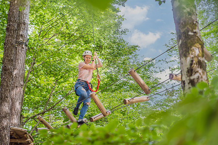 滑索摄影照片_快乐的女女孩在森林中的极限公路电车滑索中滑翔攀爬，在树上的登山扣安全链接上到树顶绳索冒险公园。