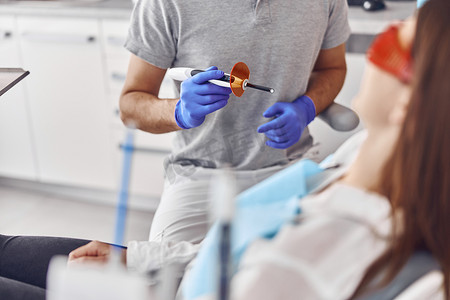 专业男医生在现代牙科柜中为快乐的白人女性补牙后使用紫外线灯