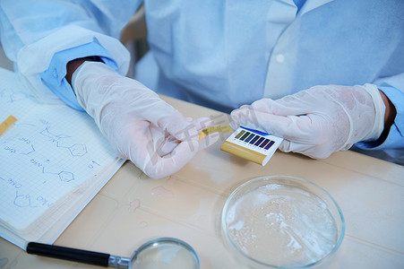 实验室助理的手使用石蕊试纸进行 PH 测试，测量培养皿中物质的酸碱度